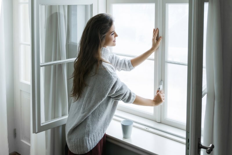 Woman in warm woolen pullover is opening window.