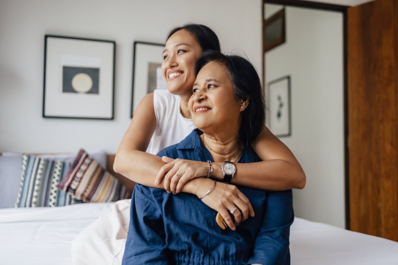 a smiling woman embracing her mother while they are looking away.